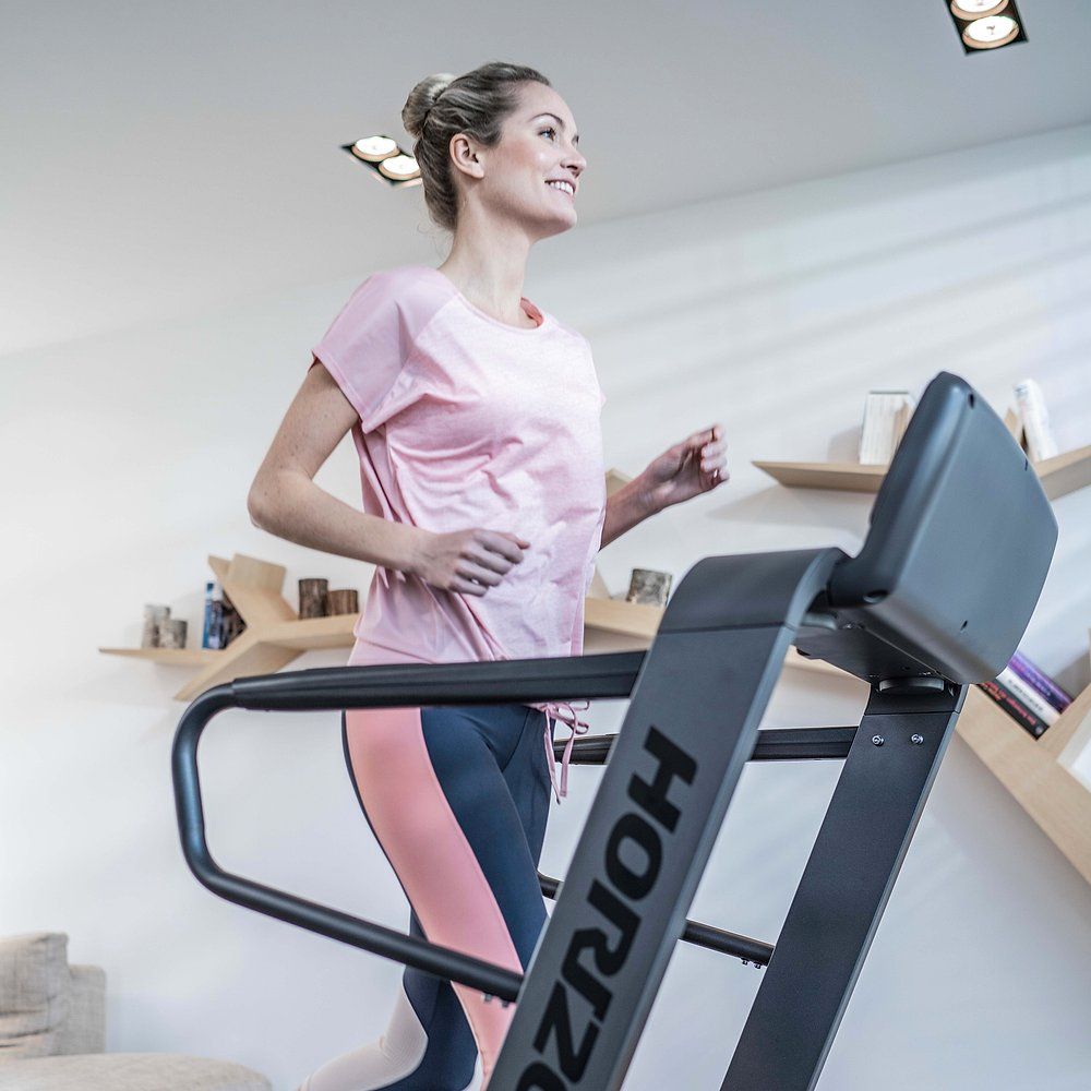 Femme courant sur un tapis roulant. Tapis roulant avec logo Horizon. La femme porte des vêtements de sport.