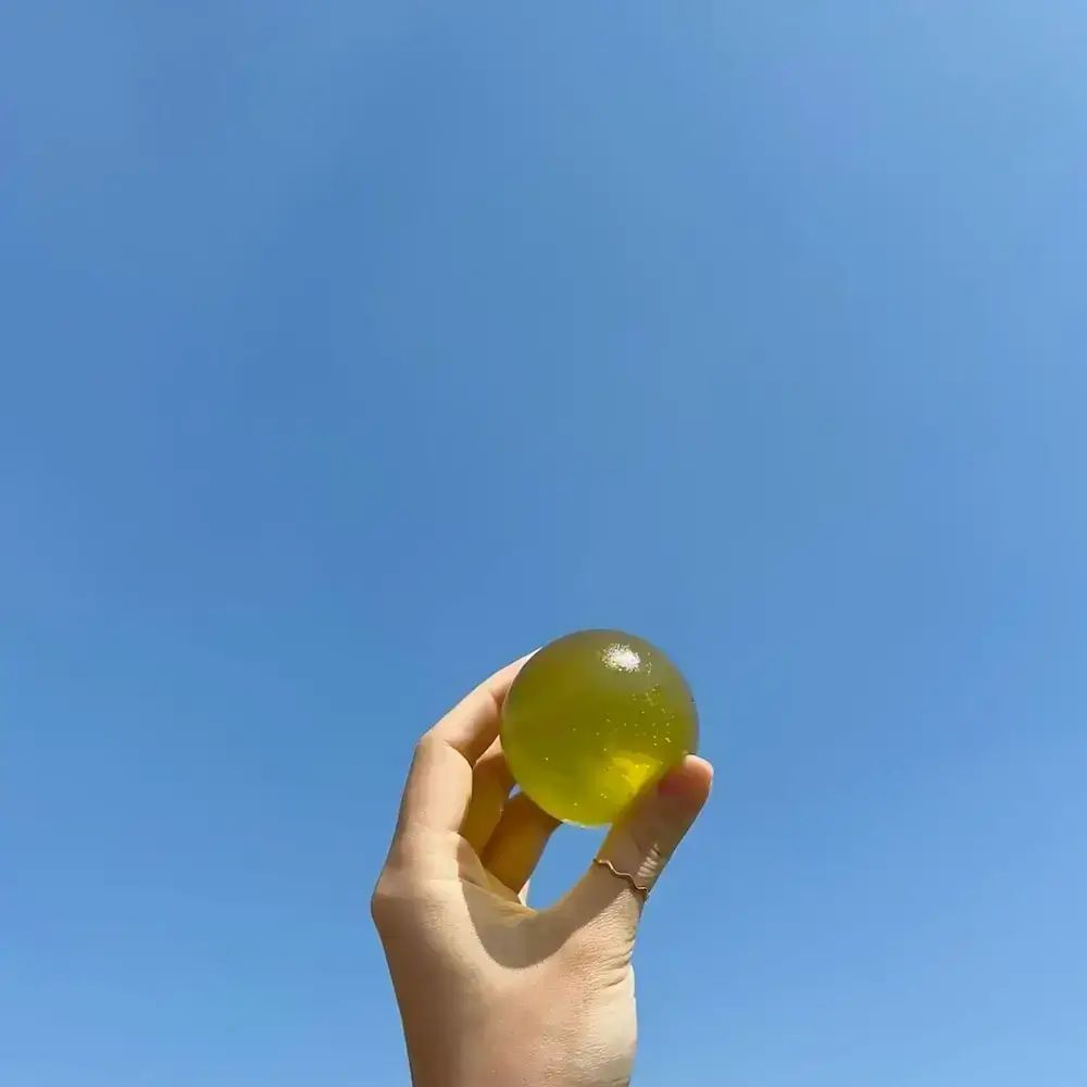 Groenachtige bal in hand, tegen blauwe lucht. Hand met ring. Heldere, ronde vorm.