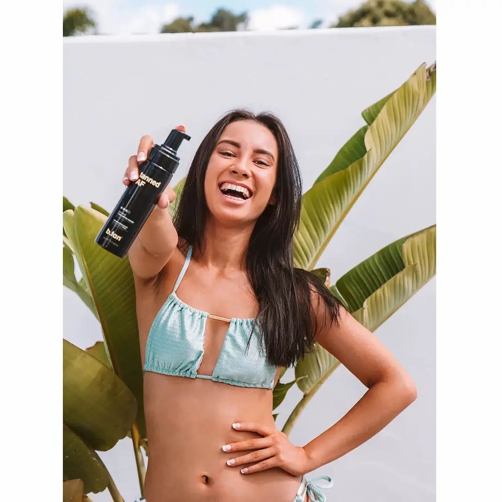 Femme tenant un flacon noir avec pompe. Inscription "tanned AF" et "b.tan".