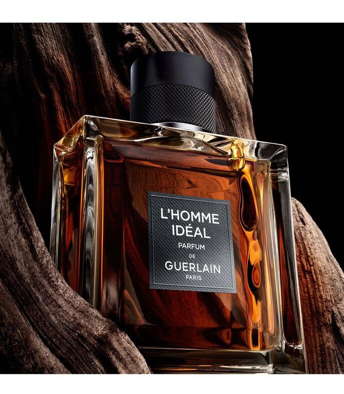 Flacon carré avec bouchon noir. Étiquette "L'HOMME IDEAL" et "GUERLAIN". Liquide brun. Devant du bois.