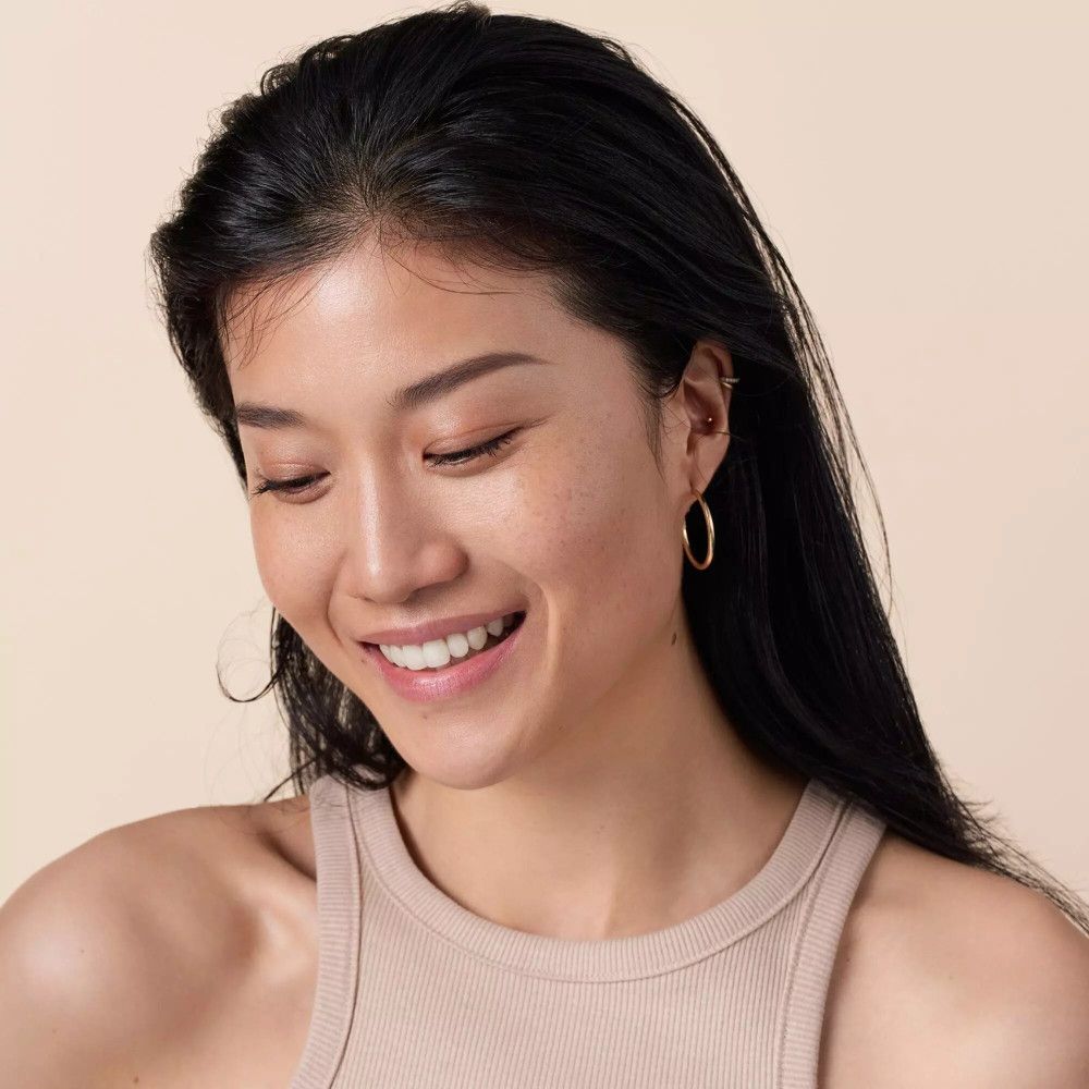 Une femme souriante aux cheveux foncés et un débardeur. Elle porte des boucles d'oreilles dorées.