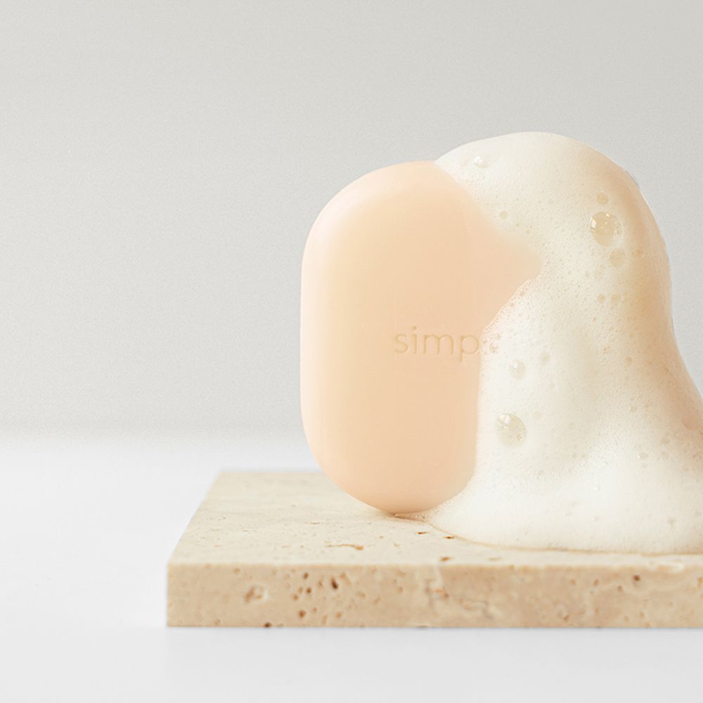 Barre de shampooing beige avec mousse. Inscription: simplyO. Placé sur une pierre.