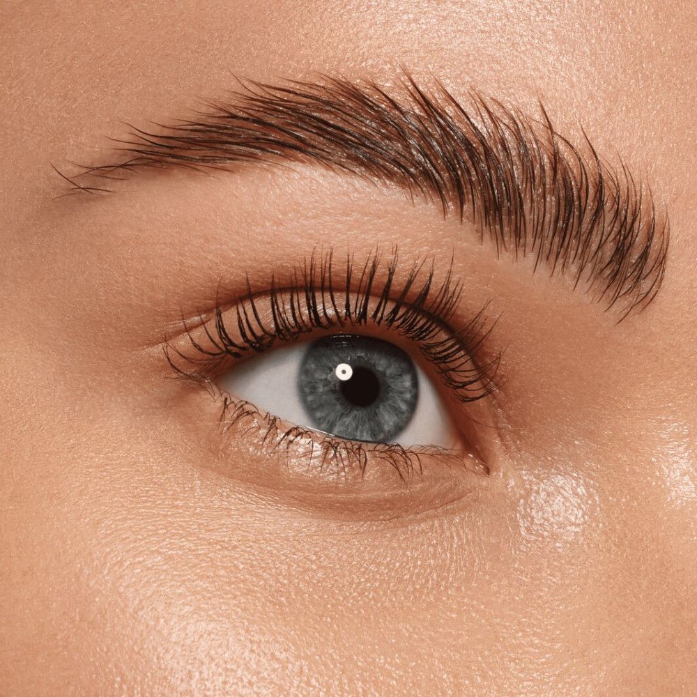 Close-up van een oog met geaccentueerde wenkbrauw. De wenkbrauw is naar boven geborsteld en lijkt voller. Blauwe ogen, lichte huid.