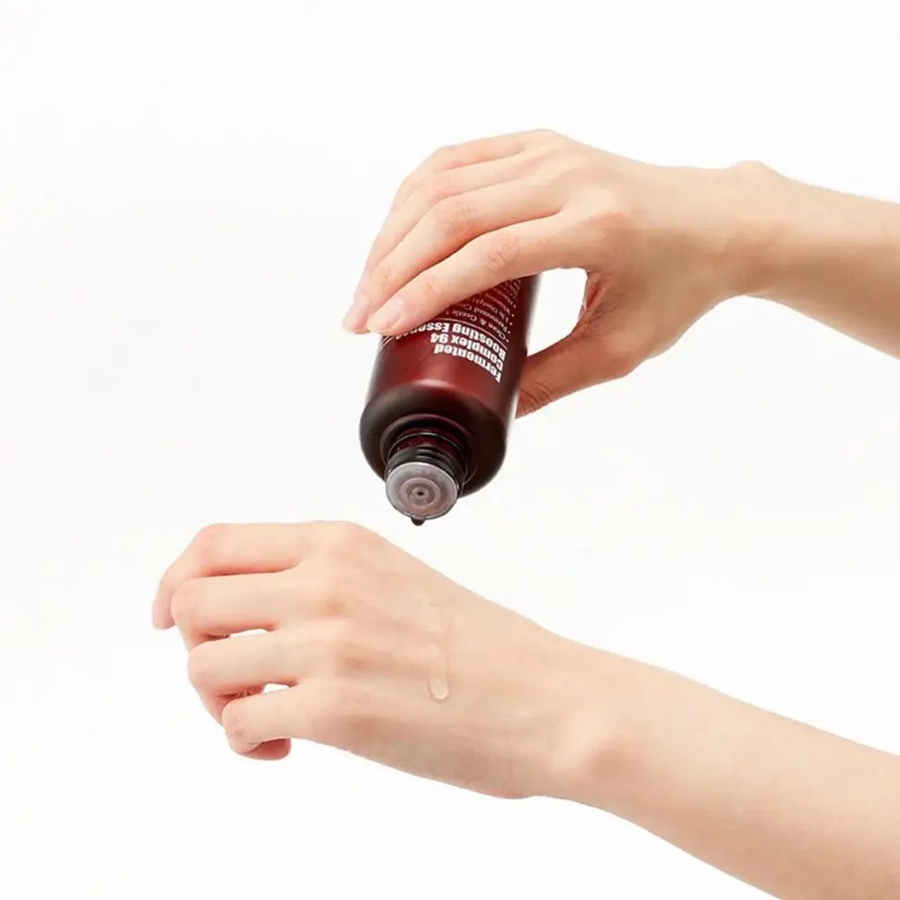 Handen houden een bruine fles vast. Vloeistof druppelt op een hand. Productnaam niet zichtbaar.