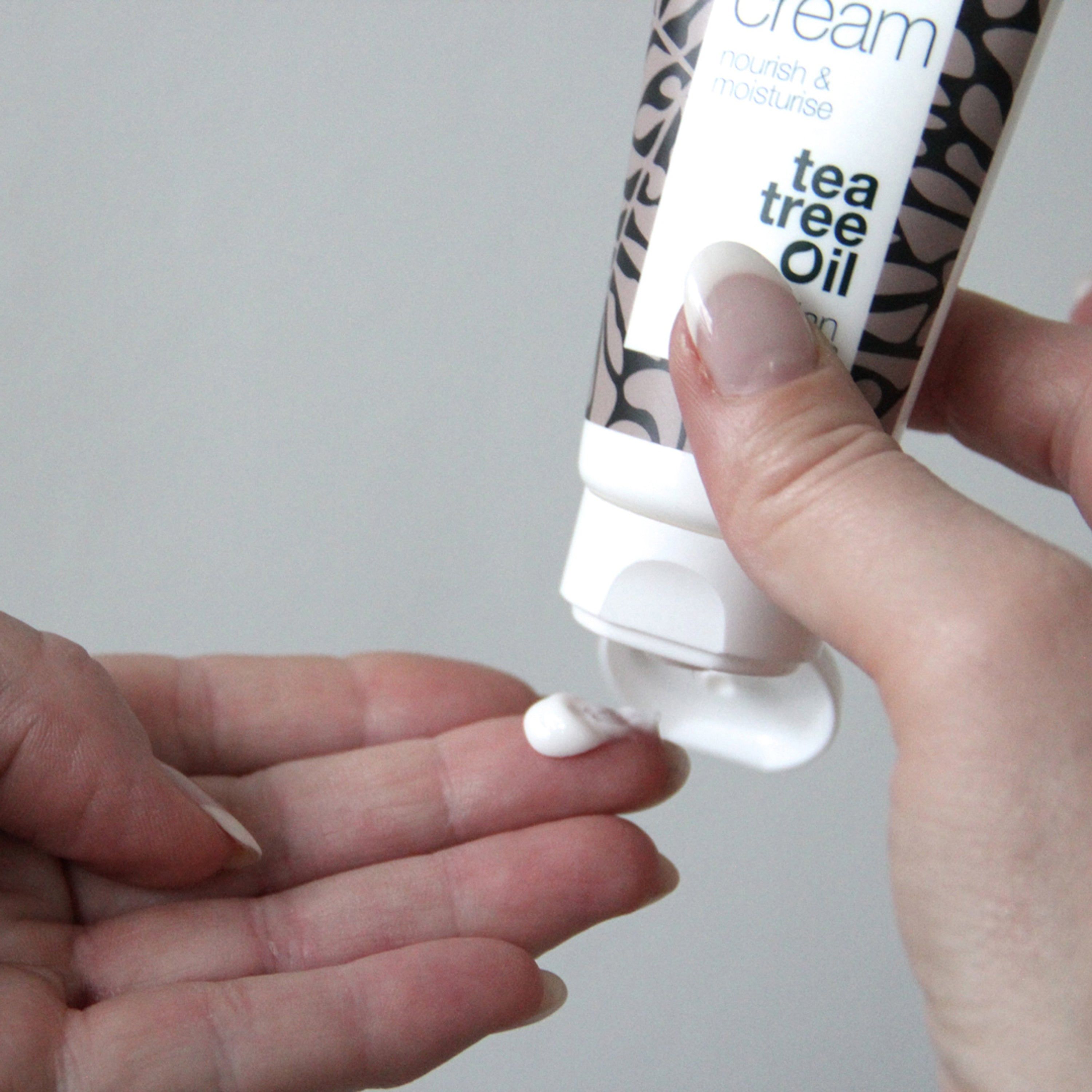 Mains avec crème. Tube avec texte : face cream, tea tree oil. Marque : Australian Bodycare. Crème sort du tube.