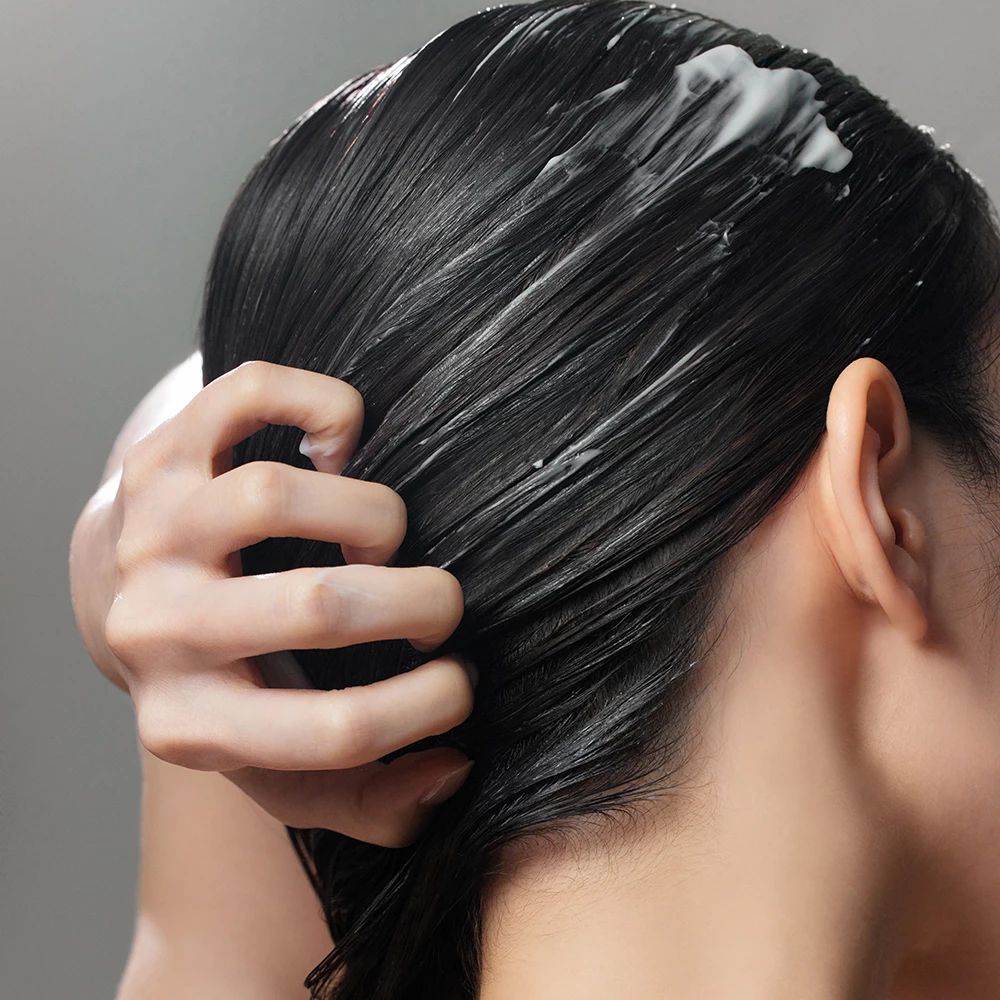 Personne avec cheveux foncés. Crème blanche sur les cheveux. Main massant. Fond gris.