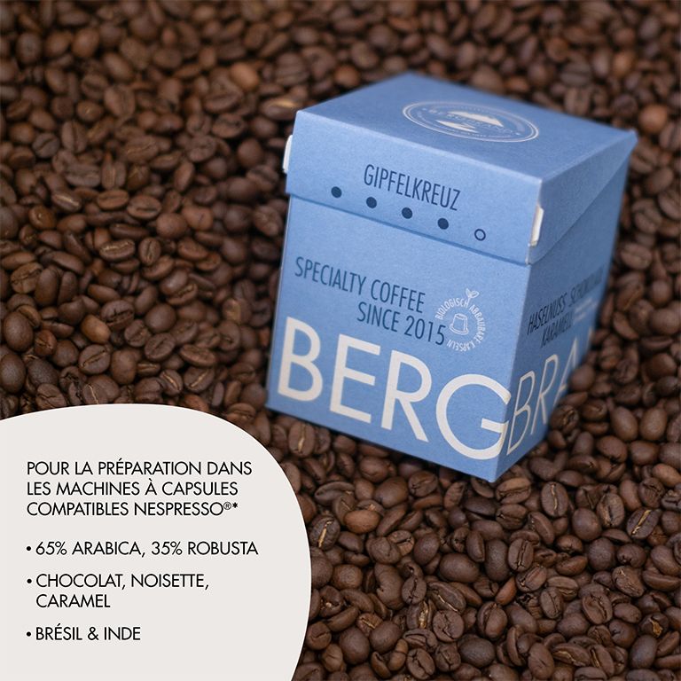 Boîte bleue avec capsules de café sur des grains de café. Texte : BERGBRAND, Gipfelkreuz, Specialty Coffee. Texte.