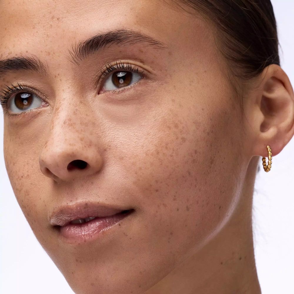 Gros plan sur un visage avec des taches de rousseur et des boucles d'oreilles dorées.