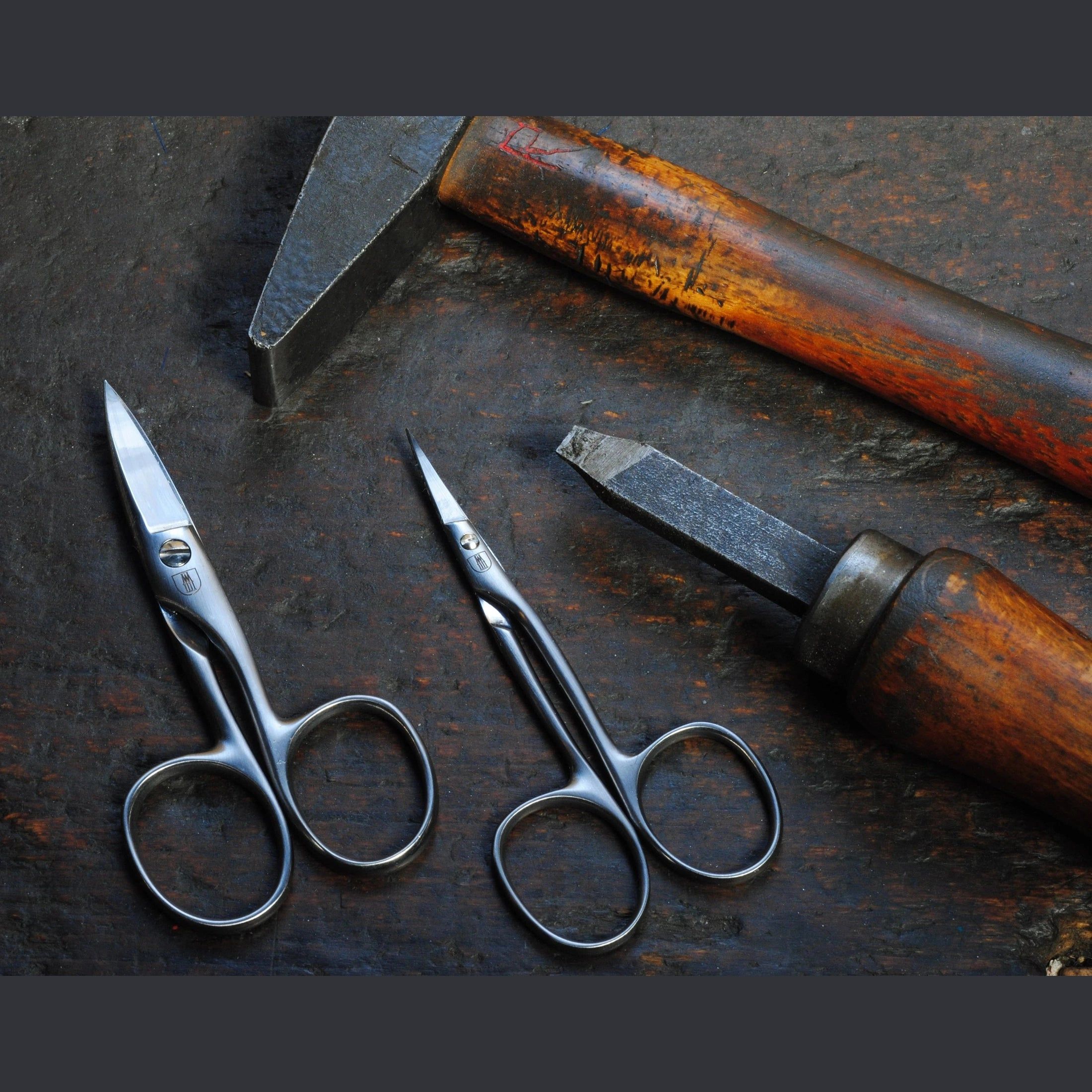 Deux ciseaux à cuticules près d'un marteau et d'un burin. Métal, lames courbes, poignées rondes.