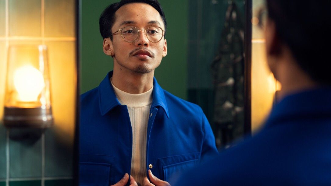 Un homme se regarde dans le miroir. Il porte des lunettes et une veste bleue.