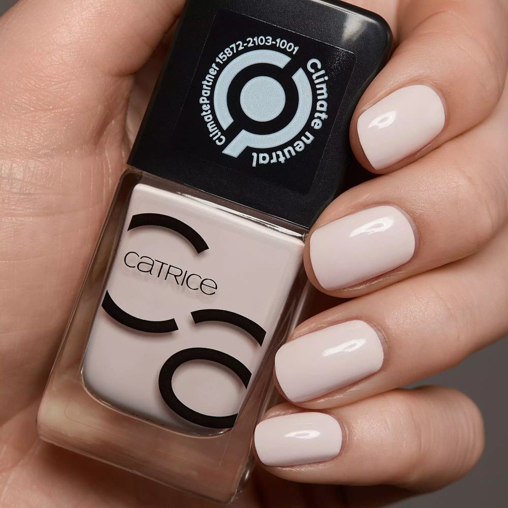 Main avec ongles vernis et flacon de vernis à ongles. Vernis à ongles Catrice Iconails rose clair.