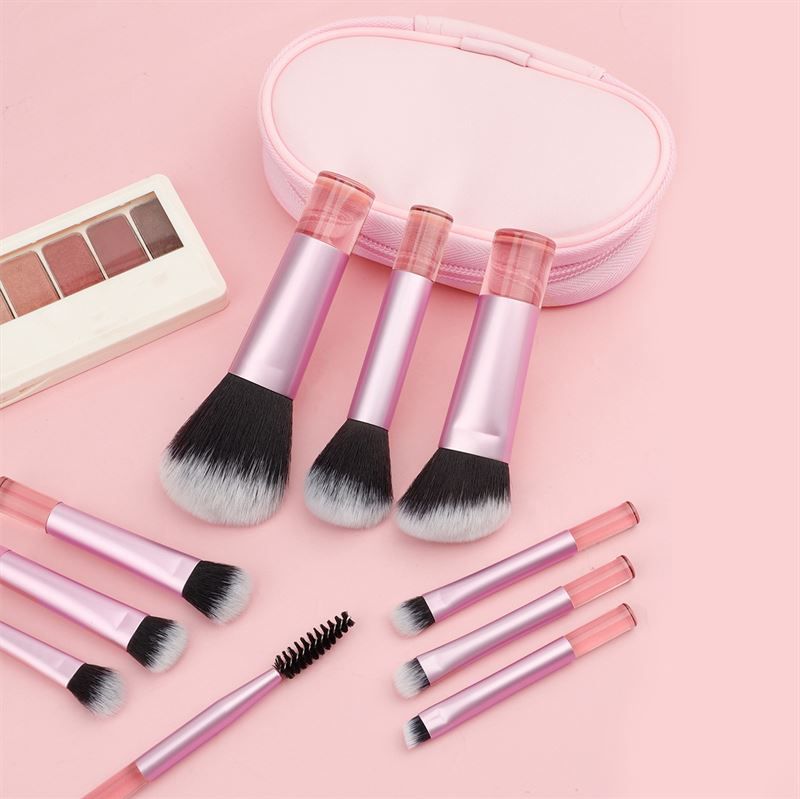 Ensemble de pinceaux avec manches roses et trousse rose. Pinceaux avec poils noirs et blancs. Quelques pinceaux sont éparpillés.