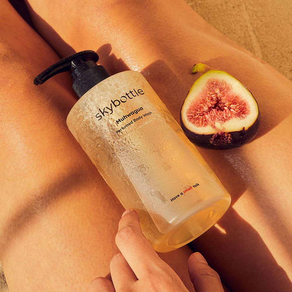 Een fles ligt op een lichaam. Daarnaast een halve vijg. Opschrift: skybottle, Muhwagua, Perfumed Body Wash.