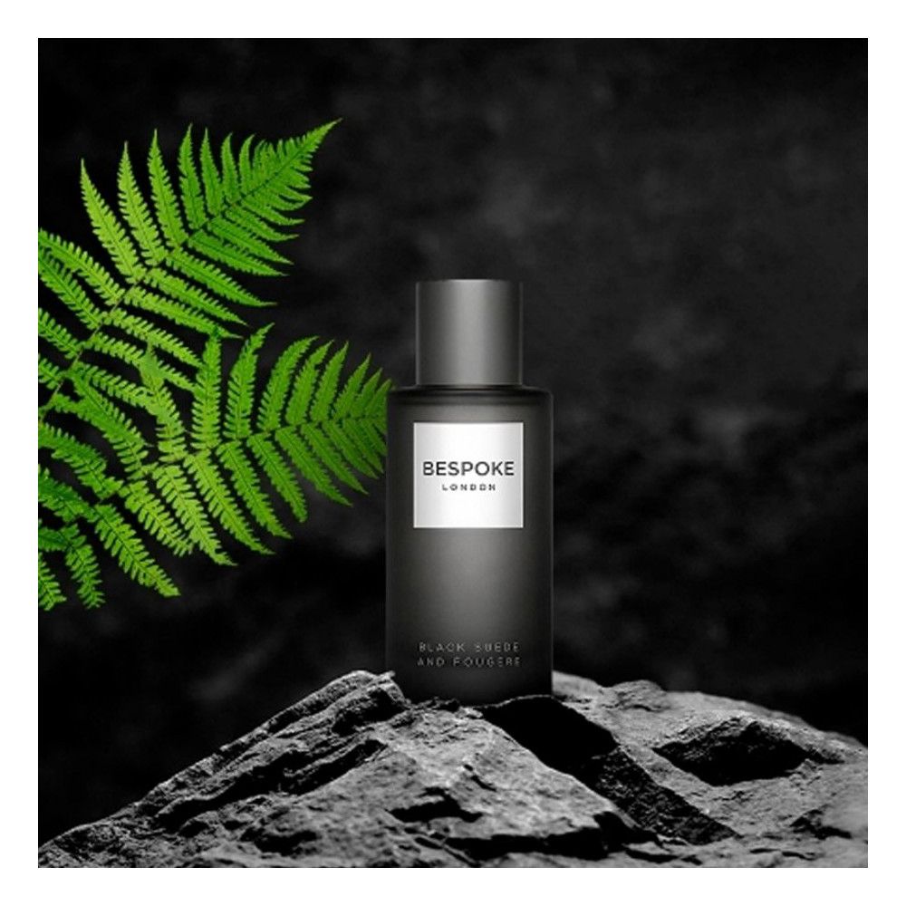 Flacon sombre sur pierre. "BESPOKE LONDON" sur étiquette blanche. Texte: "BLACK SUEDE AND FOUGERE". Feuille verte en arrière-plan.