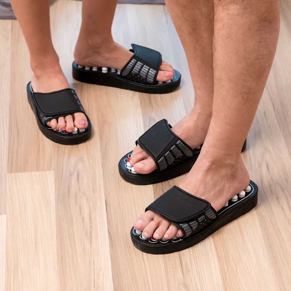 Drie personen dragen acupressuurschoenen. Zwarte schoenen met witte en rode noppen. Verstelbare riem.
