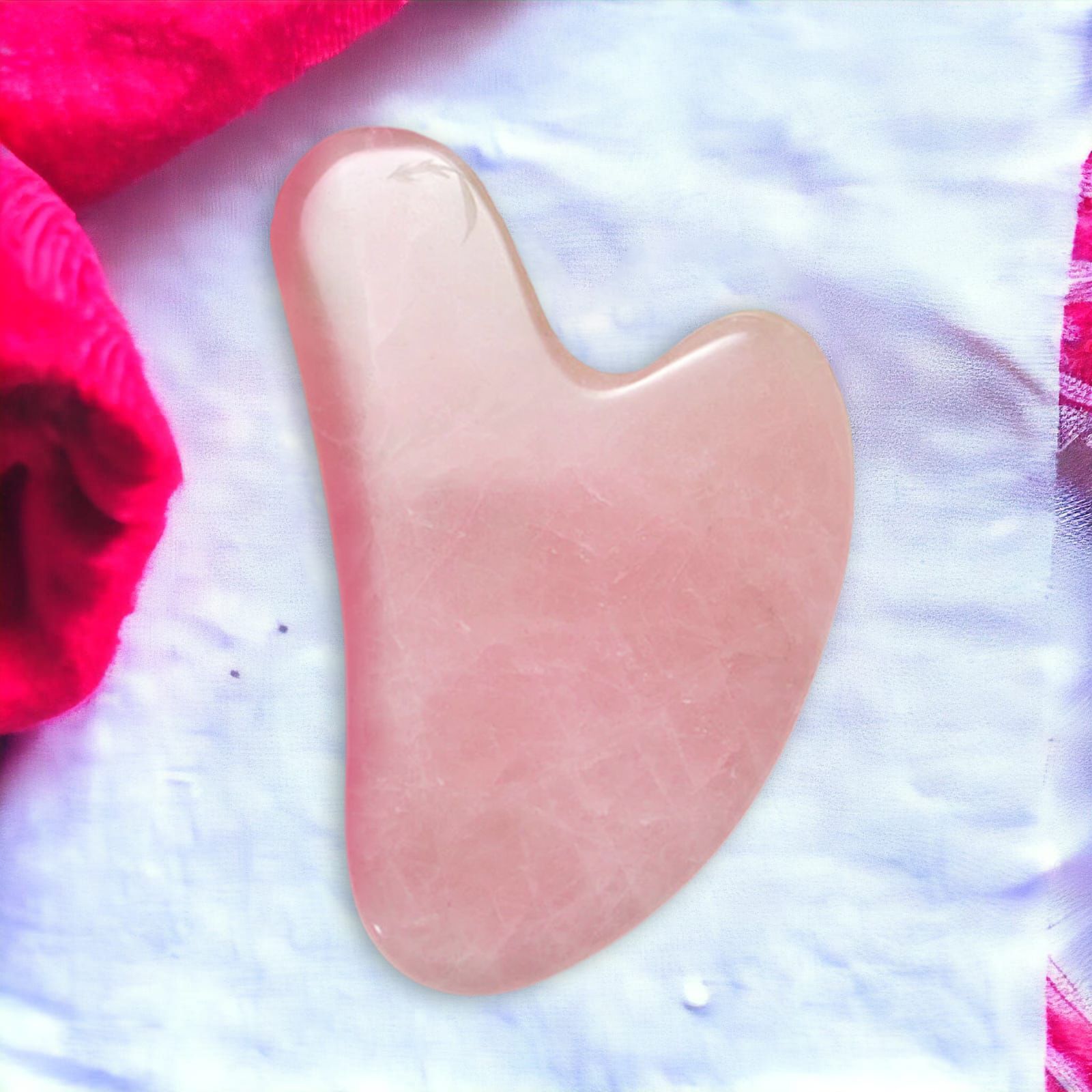 Gua Sha rose en pierre, en forme de cœur. Sur tissu blanc, à côté d'une serviette rouge.