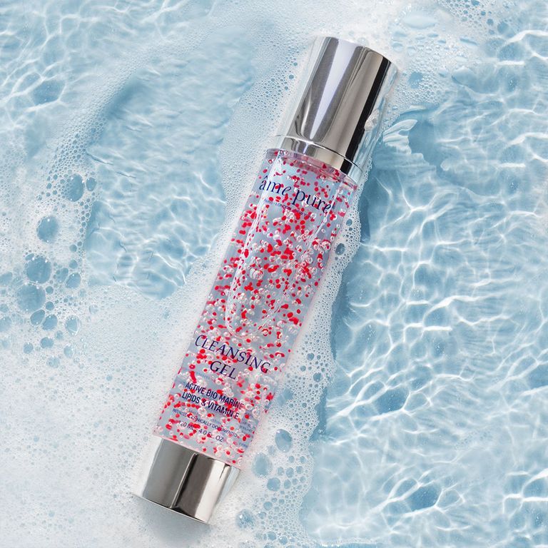 Un flacon de gel nettoyant avec particules rouges flotte dans de l'eau pétillante.