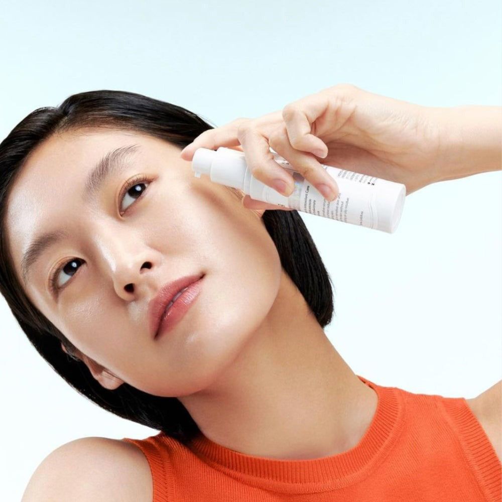 Vrouw houdt een witte fles tegen haar wang. Product: klairs Freshly Juiced Charging Serum. Huidverzorging.