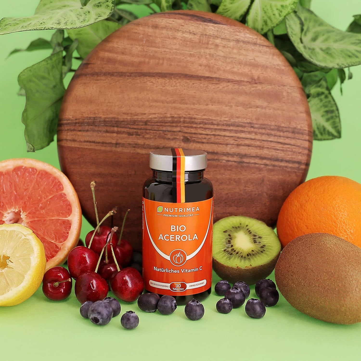 Bruine glazen fles met oranje etiket, met opschrift "BIO ACEROLA Natuurlijke Vitamine C". Omringd door fruit: kersen, bosbessen, kiwi, sinaasappel, citroen.