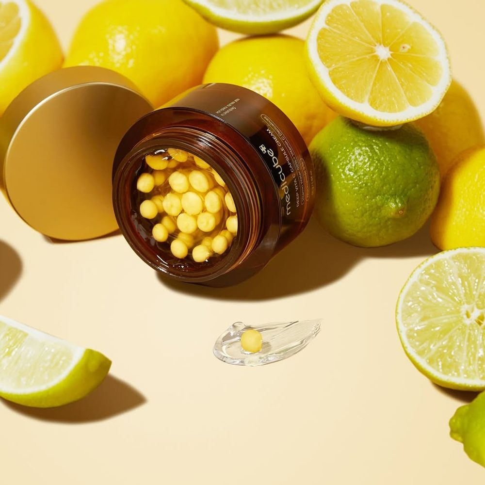 Product met open deksel, gele capsules. Citroenen en limoenen op de achtergrond.