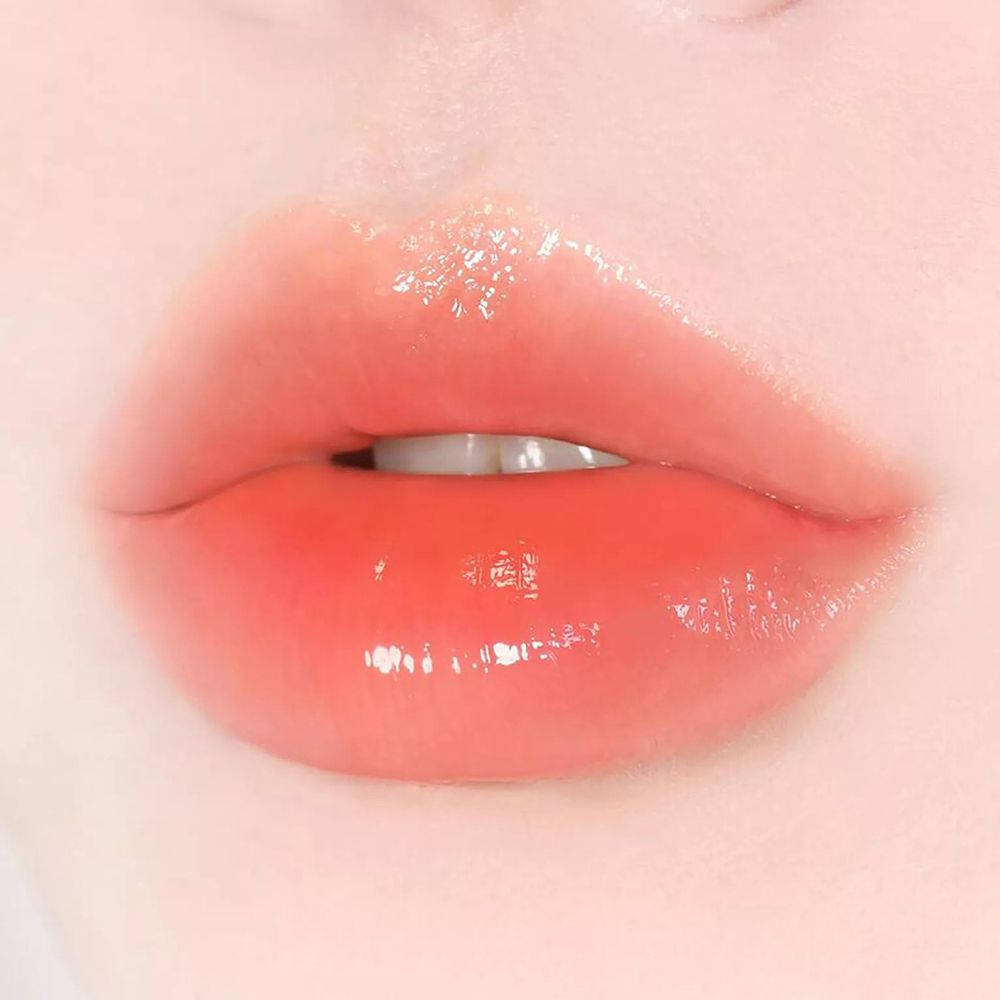 Close-up van lippen met glanzende, oranje lippenbalsem. De lippen zijn lichtjes geopend.