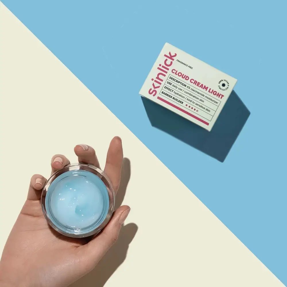 Main tenant un pot ouvert de gel bleu. À côté, boîte avec inscription Cloud Cream Light. Fond: bleu/jaune.