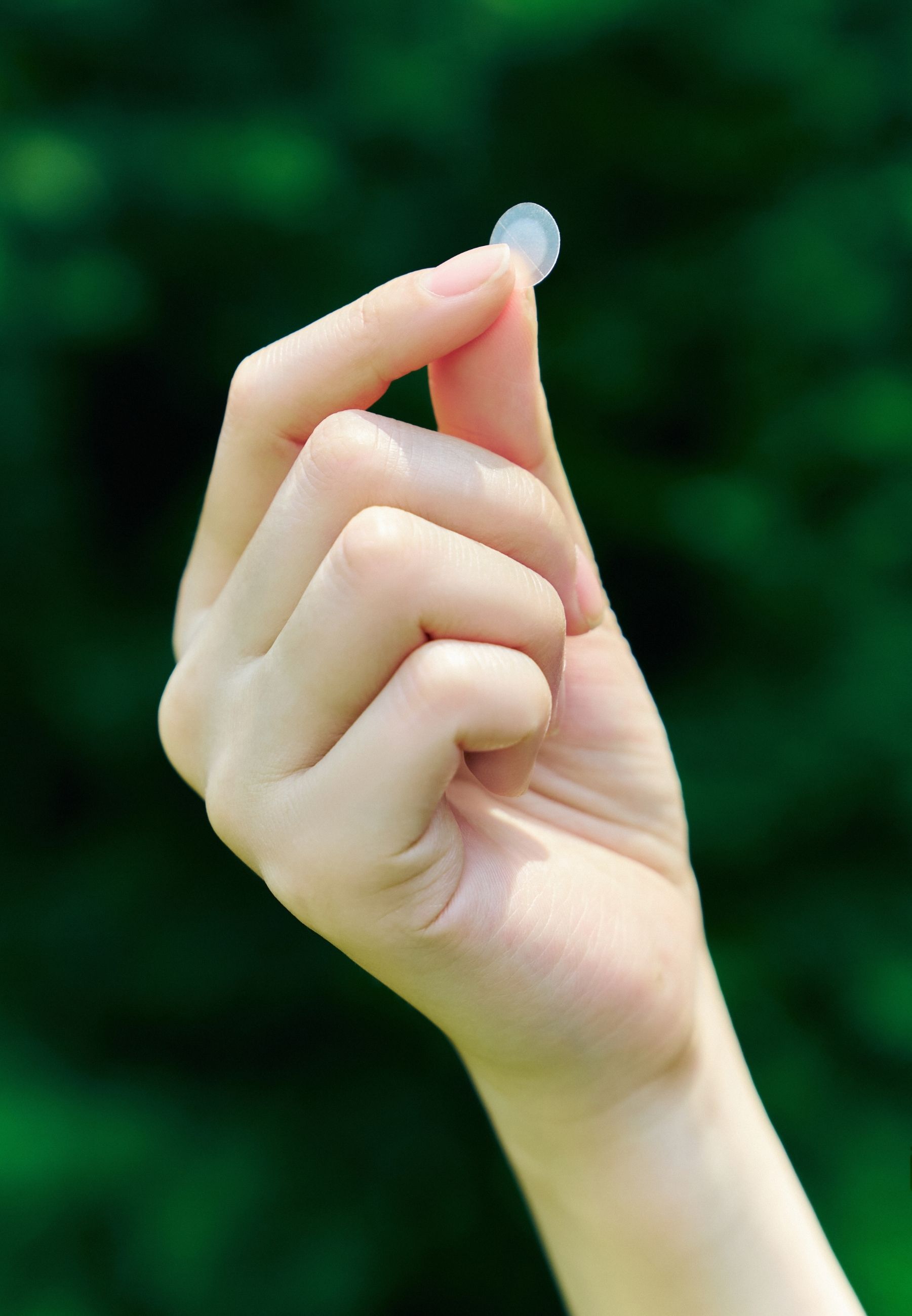 Hand houdt een transparante, ronde patch vast. Groene achtergrond.