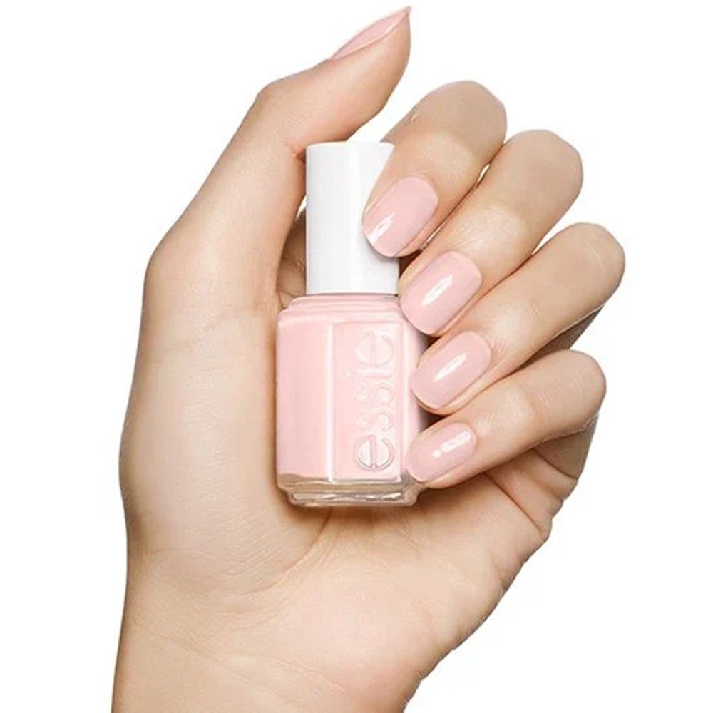 Main tenant un flacon de vernis à ongles Essie rose pâle.