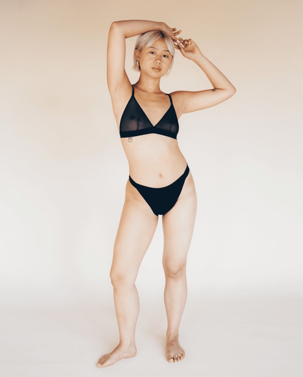 Culotte bikini noire et soutien-gorge. Femme blonde, bras levés. Tissu transparent.