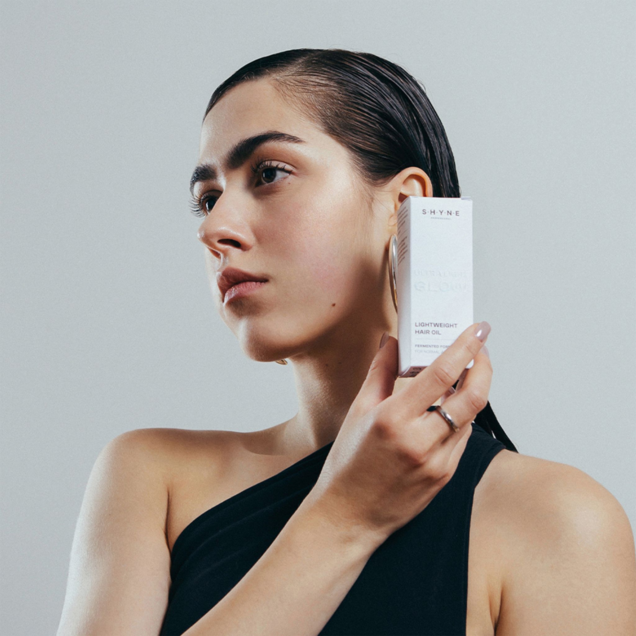 Femme tenant une boîte avec l'inscription SHYNE. Sur la boîte: LIGHTWEIGHT HAIR OIL.