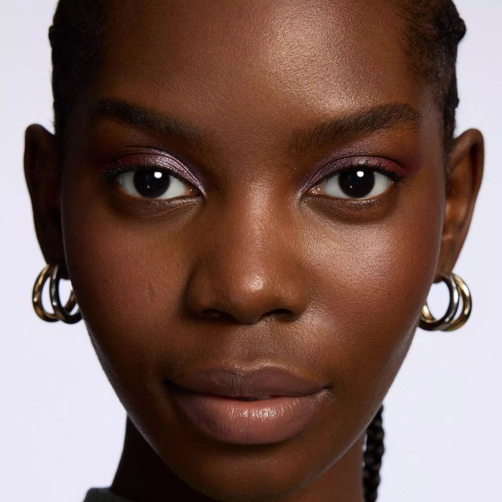 Portrait d'une femme à la peau foncée avec fard à paupières rose. Boucles d'oreilles dorées. Pas de nom de produit ni de marque.