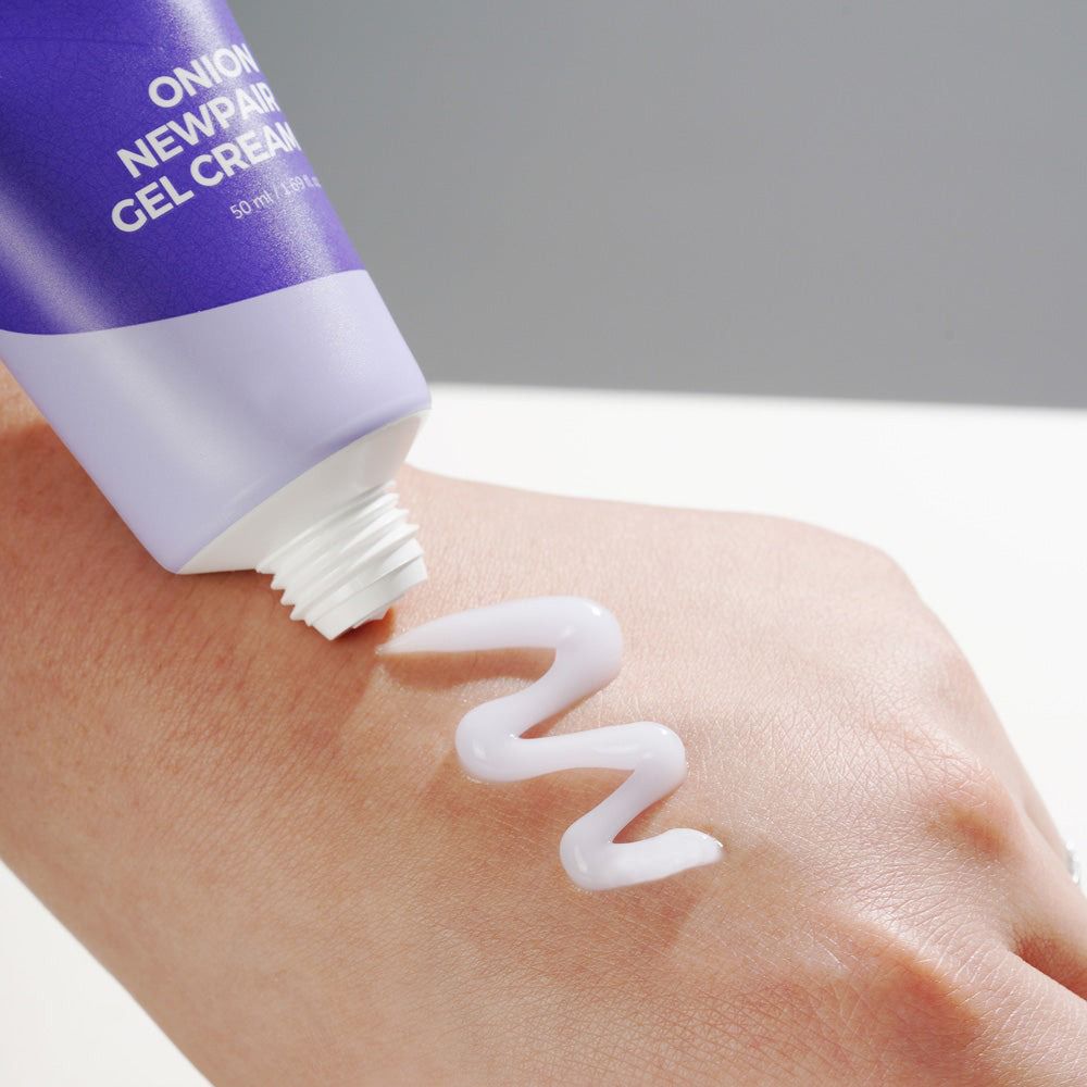 Hand met crème. Tube met tekst: ONION NEWPAIR GEL CREAM. Crème wordt uitgeknepen. Witte, golvende crème.