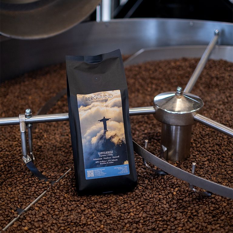 Sachet noir de café BERGBRAND Gipfelkreuz. Inscription et image du Christ Rédempteur. Grains de café en arrière-plan.