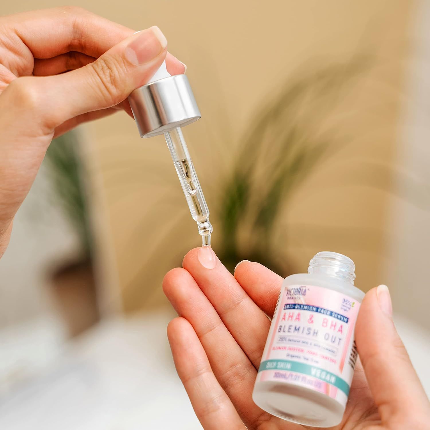 Een hand houdt een pipet met serum boven een andere hand die een klein flesje AHA & BHA Blemish Out serum vasthoudt.