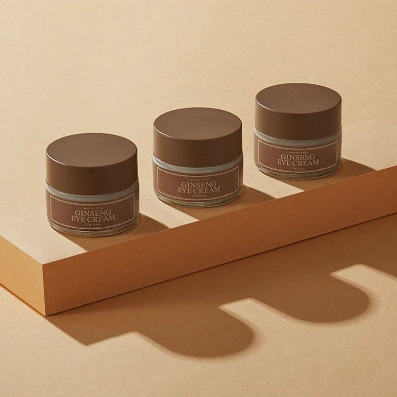 Drie oogcrème potjes met bruine deksels. Tekst: Ginseng Eye Cream, I'm from. Op sokkel.