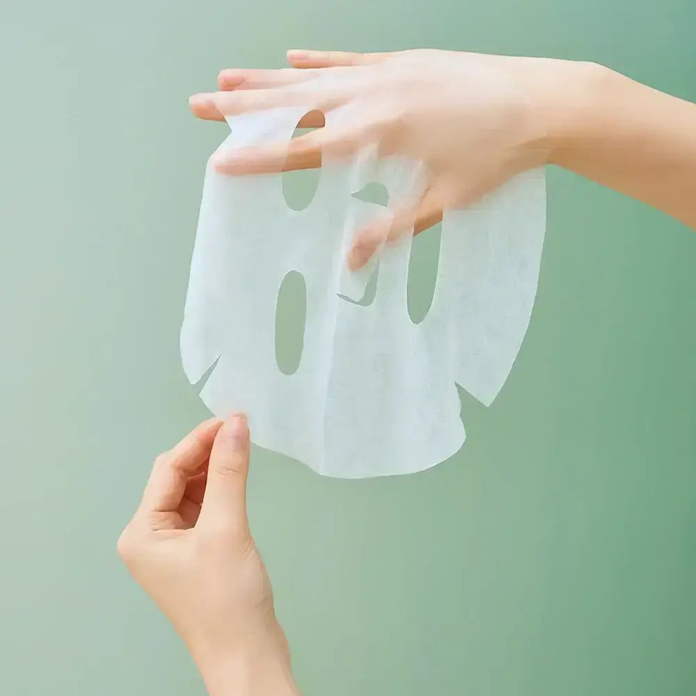 Masque facial blanc, avec ouvertures pour les yeux, le nez et la bouche. Mains tenant le masque sur fond vert.