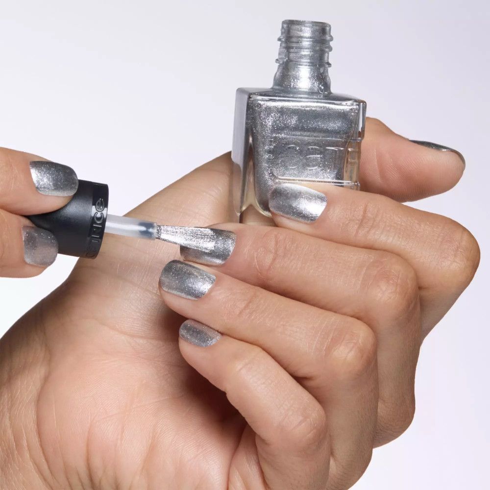 Main avec ongles vernis argentés. Flacon de vernis à ongles avec pinceau. Marque Catrice.