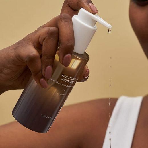 Hand houdt fles met pomp vast. Olie druppelt uit de dispenser. Opschrift: haruharu wonder Black Rice Moisture Deep Cleansing Oil.