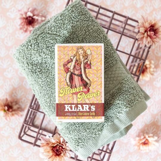 Klar's zeep, verpakt, op een mand met handdoek. Opdruk: Flower Power, vrouw met zeep. Onder: Klar's, zeep uit de jaren 70.
