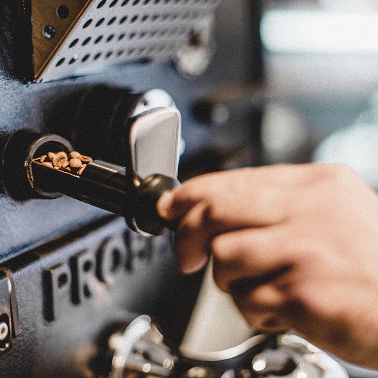 Une main prélève des grains de café d'une torréfactrice.