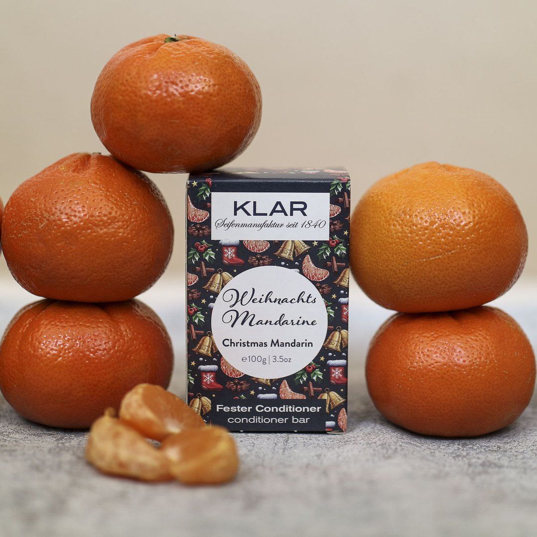 Emballage de barre revitalisante Klar-Seifen entre des mandarines. Mandarines sur et à côté de l'emballage. Texte : "Weihnachts Mandarine", "Fester Conditioner".