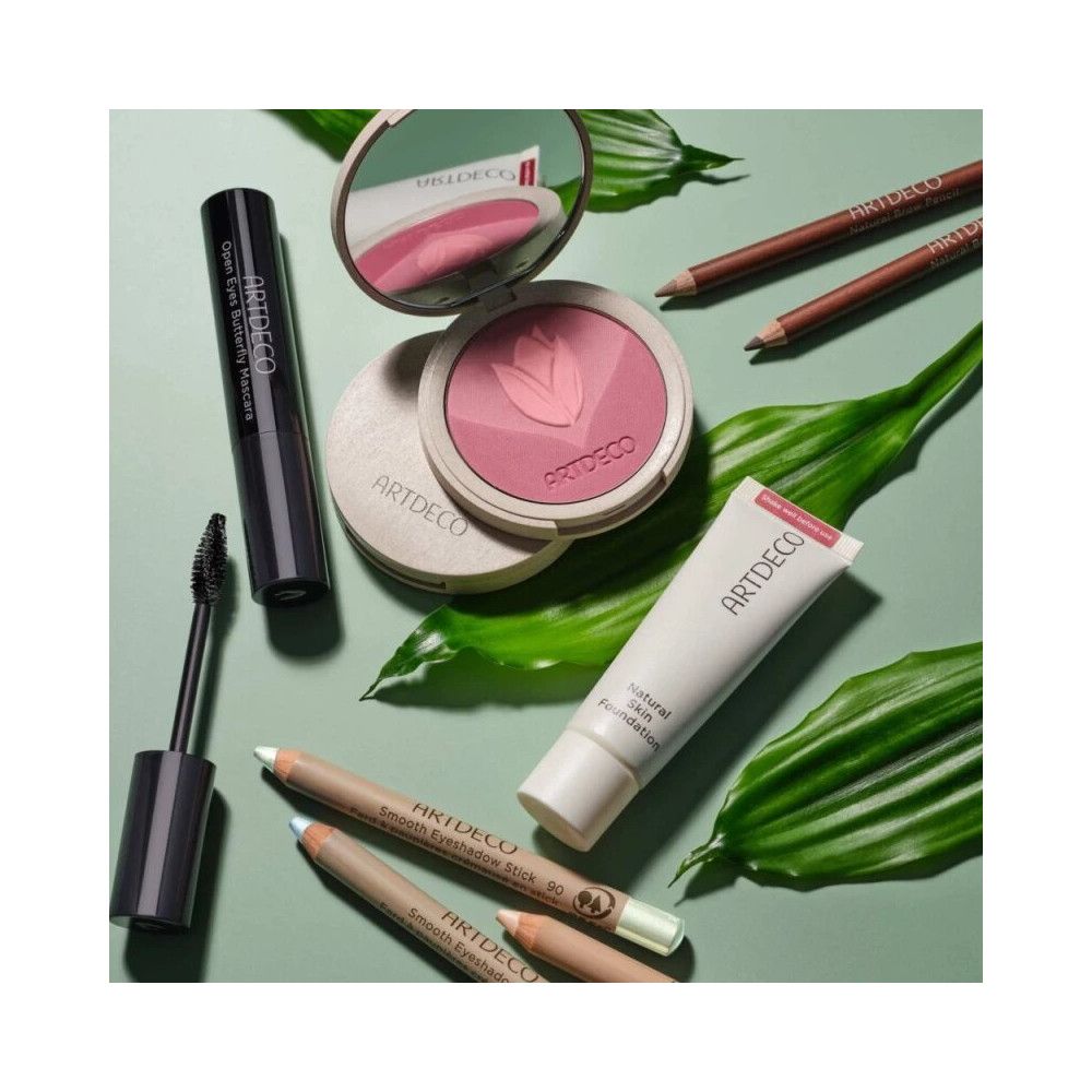 Cosmetica op groene achtergrond. Inclusief: mascara, poeder, foundation, wenkbrauwpotloden. Artdeco-logo zichtbaar.