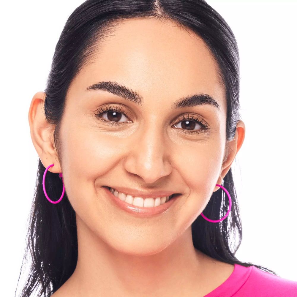 Portrait d'une femme avec des boucles d'oreilles roses. Elle sourit à la caméra. Teint uniforme.