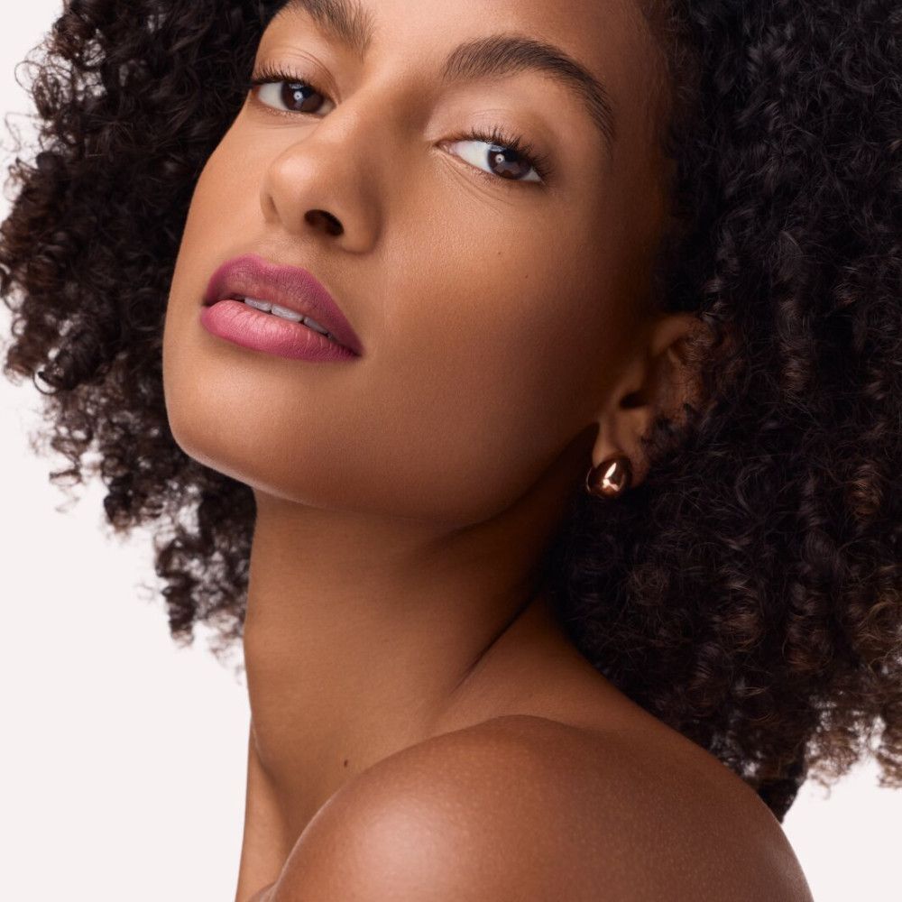 Portrait d'une femme aux cheveux bouclés et au rouge à lèvres. Elle porte des boucles d'oreilles dorées.