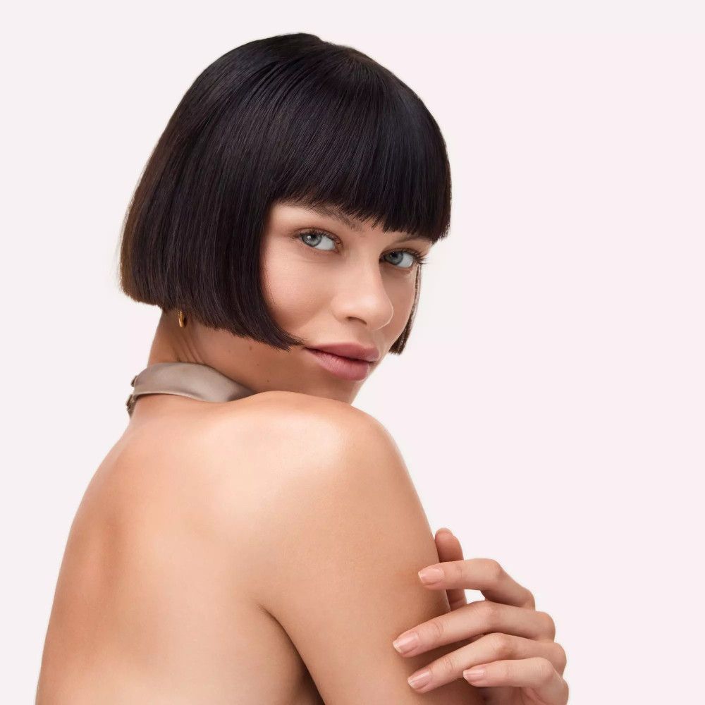 Portrait d'une femme avec une coupe au carré. Elle porte un haut beige et regarde de côté.