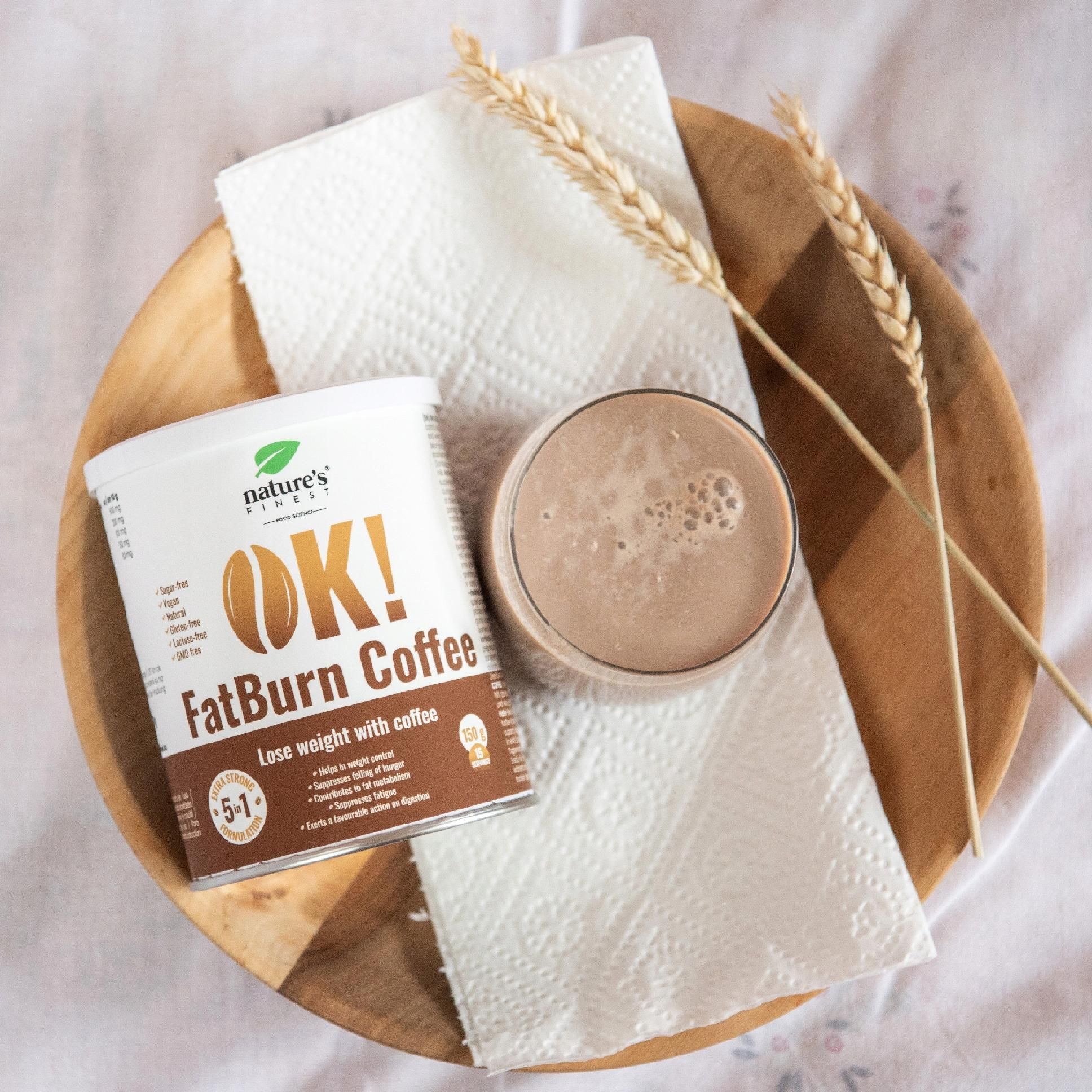 Boîte OK! FatBurn Coffee à côté d'une tasse de café sur une assiette en bois.