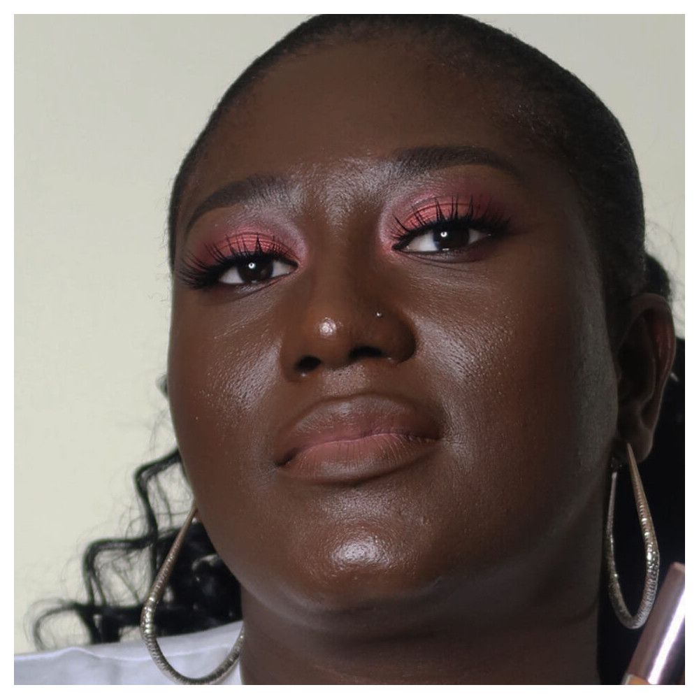 Gros plan d'une personne maquillée. Fard à paupières rose, peau foncée, boucles d'oreilles.