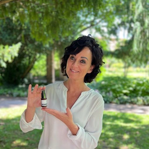 Femme tenant un flacon de produit. Texte: Anti-Aging Eye Contour Cream. Fond: arbre vert, journée ensoleillée.