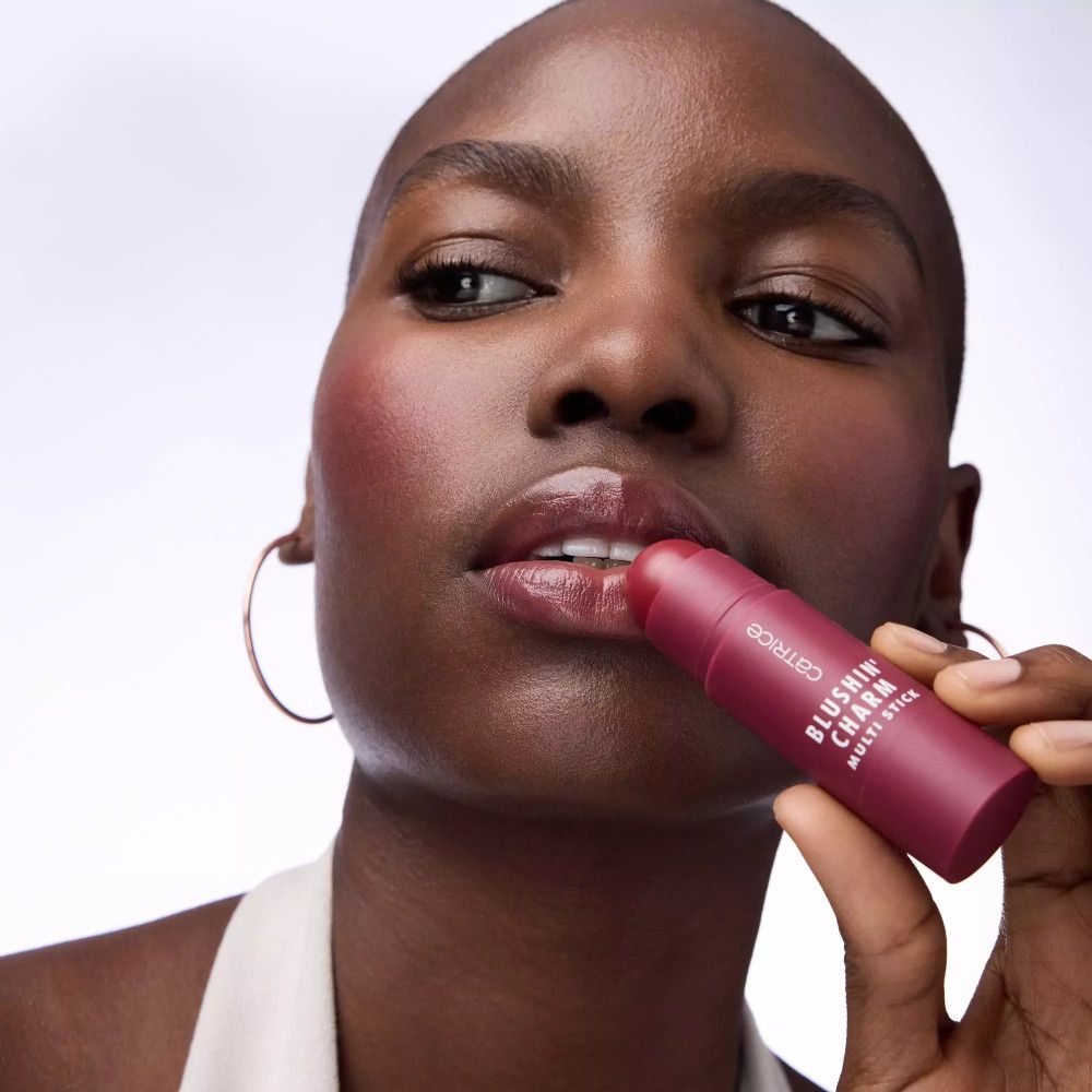 Femme avec un stick de blush sur les lèvres. Inscription: CATRICE, BLUSHIN' CHARM, MATTE STICK.