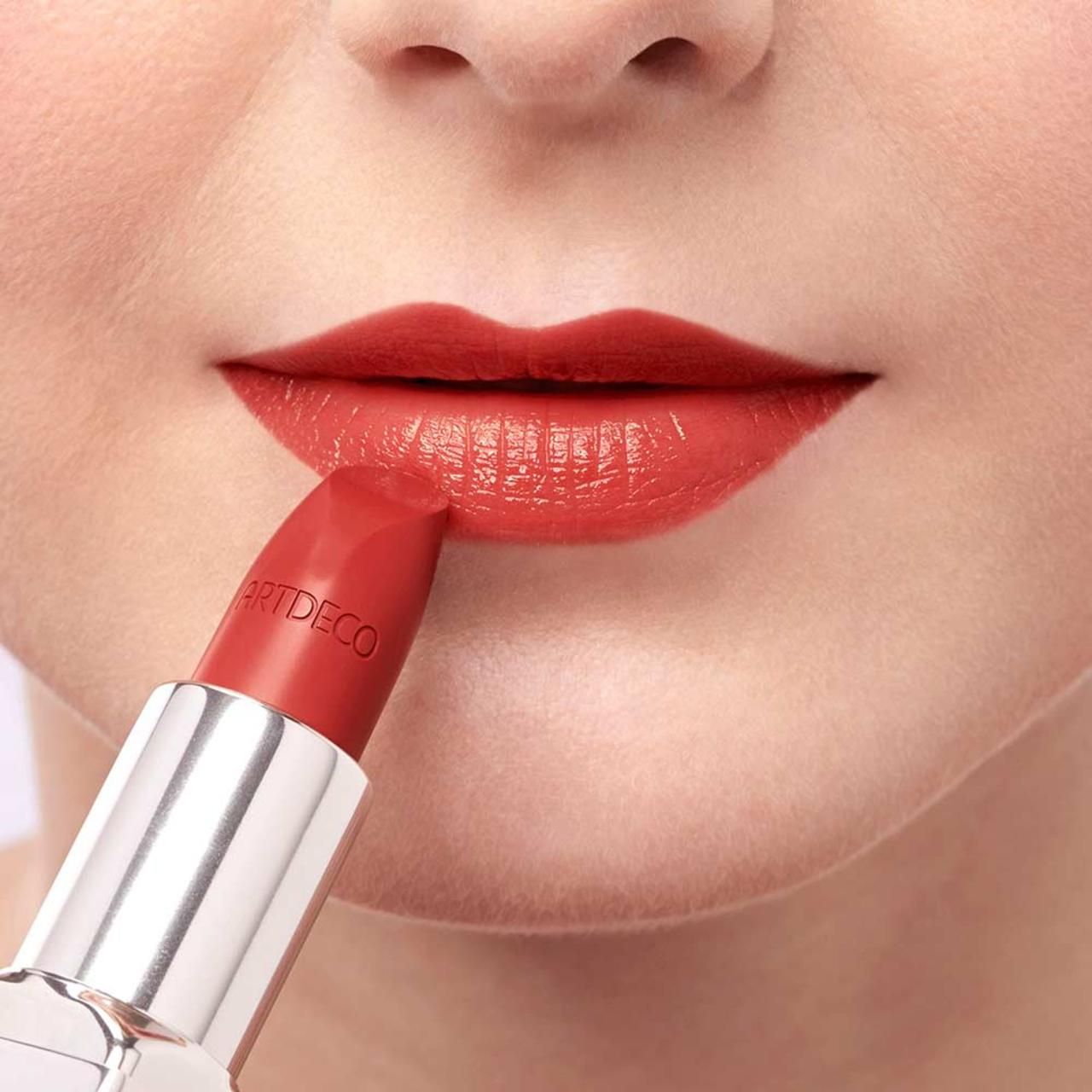 Persoon brengt rode lipstick aan. De lipstick draagt de tekst ARTDECO.